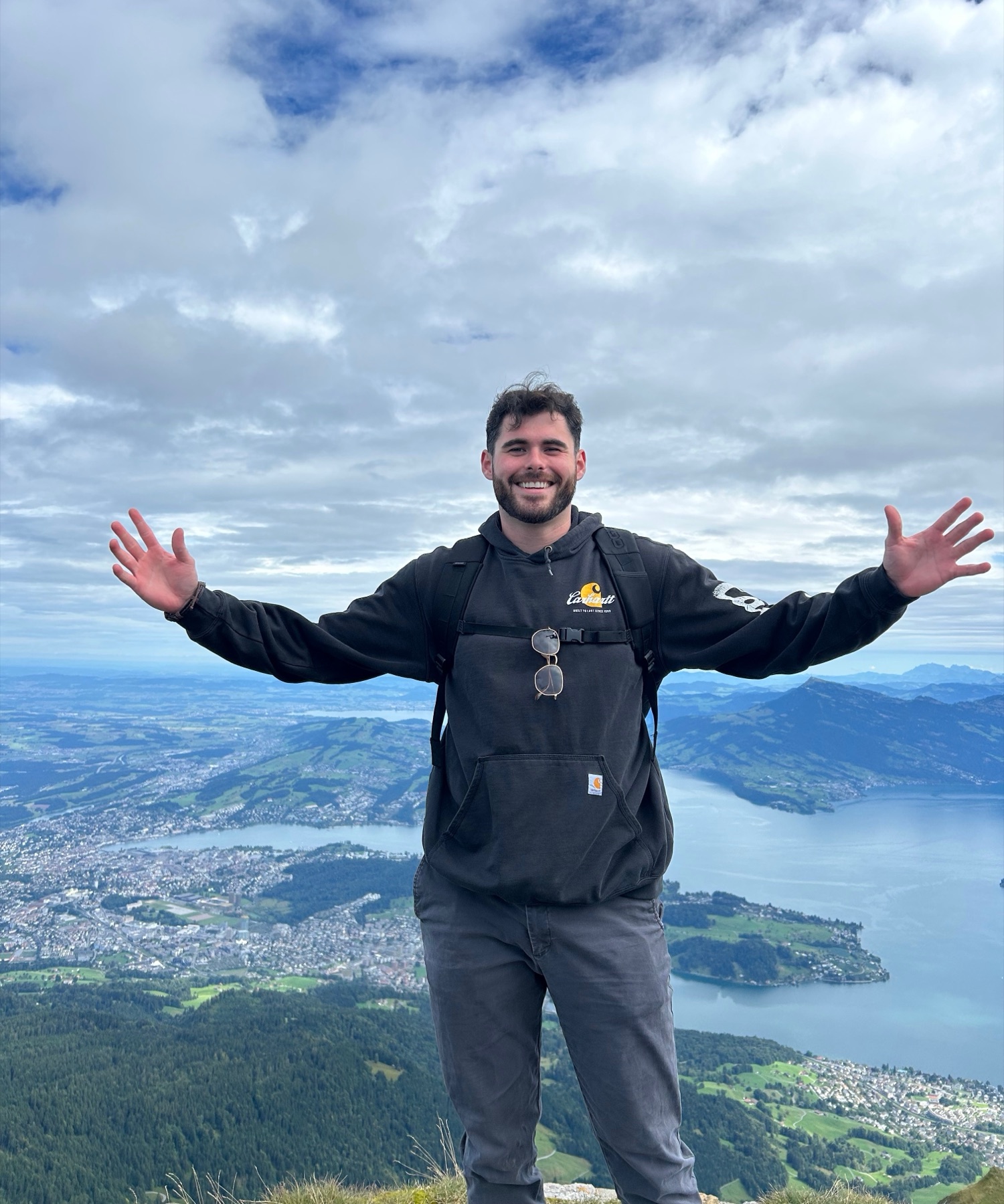 Alex Petrakes on a mountain above an alpine lake, arms spread